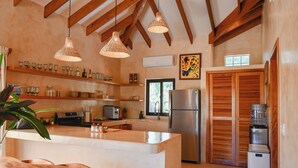 Une cuisine avec des poutres en bois, un îlot central, des luminaires suspendus et un réfrigérateur.