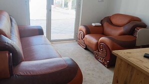 Una sala de estar con dos sofás de cuero marrón, una mesa de centro de madera y un portón corredizo de vidrio que da a un espacio al aire libre.