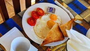 Un plato de desayuno con huevos, tostadas, tomates y un recipiente pequeño con mantequilla.