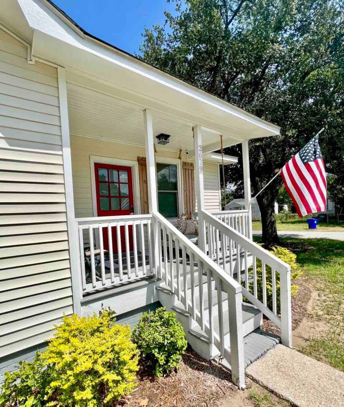 A single-story house with a porch, a red door, and an American flag.
