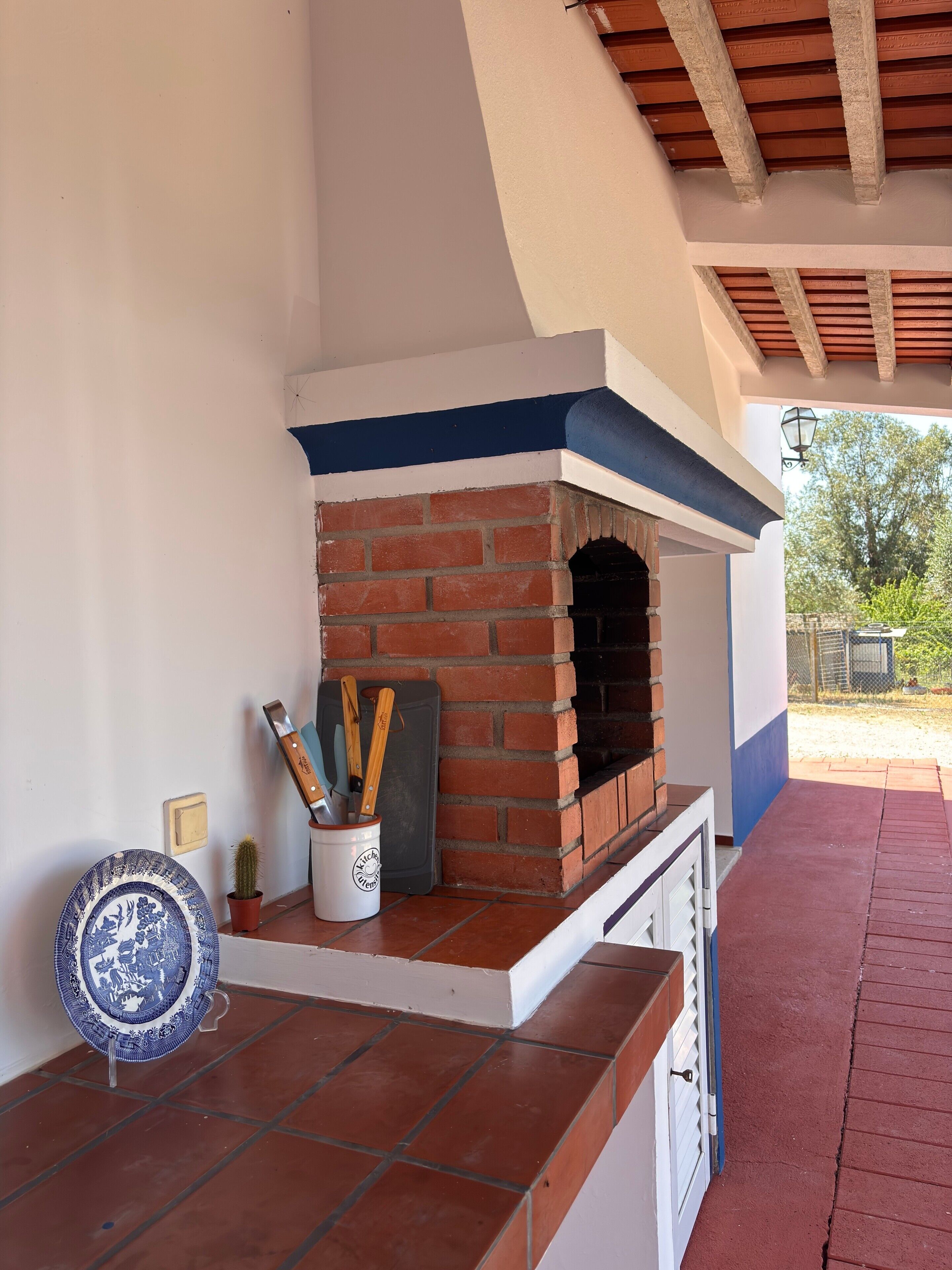 Un horno de ladrillo con exterior blanco y azul, piso de baldosas y una maceta con un cactus.