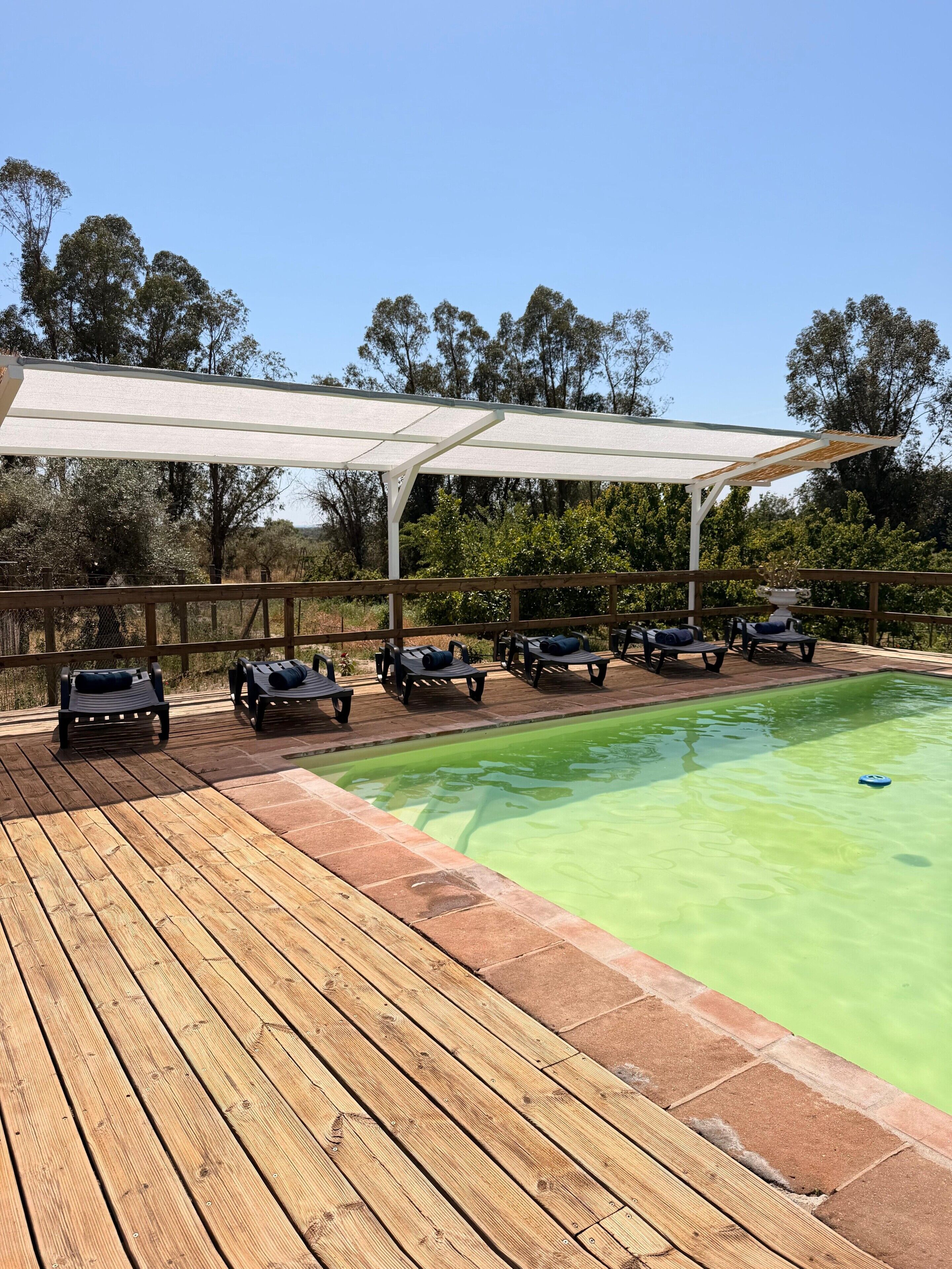 Ein Poolbereich mit Holzterrasse, Liegestühlen und einer überdachten Sitzgruppe.