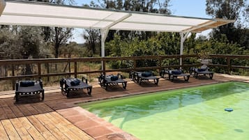 Ein Poolbereich mit Holzterrasse, Liegestühlen und einer überdachten Sitzgruppe.