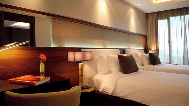 A hotel room with two beds, a desk with a lamp, a chair, a book, and a mirror. - F Shasa Vela Condominium (Koh Samui)
