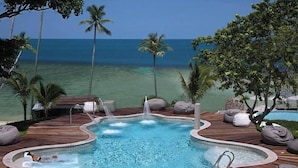 A pool with a wooden deck, surrounded by bean bags and palm trees, overlooking the ocean. - F Shasa Vela Condominium (Koh Samui)