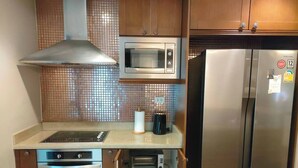 A compact kitchen with a stove, microwave, oven, and refrigerator. - F Shasa Vela Condominium (Koh Samui)