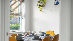 A dining table set with plates, bowls, and wine glasses, with yellow chairs and a window with blinds. - Drakeway House, Reading (Berkshire)