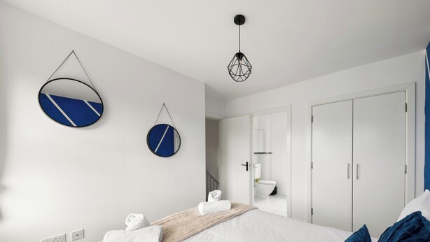 A modern bedroom with a bed, two wall-mounted mirrors, a wardrobe, and a hanging light fixture. - Drakeway House, Reading (Berkshire)