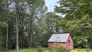 Una cascina rossa circondata da alberi fitti e un prato curato.