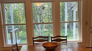Una sala da pranzo con tavolo e sedie in legno, ampie finestre con vista sugli alberi e un decoro a stella sul davanzale.