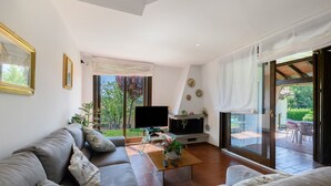 Ein modernes Wohnzimmer mit einer Couch, einem Fernseher und einer Schiebetür zu einer Terrasse.