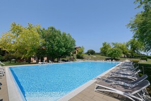 Una piscina con sillas de descanso, árboles y un edificio al fondo.