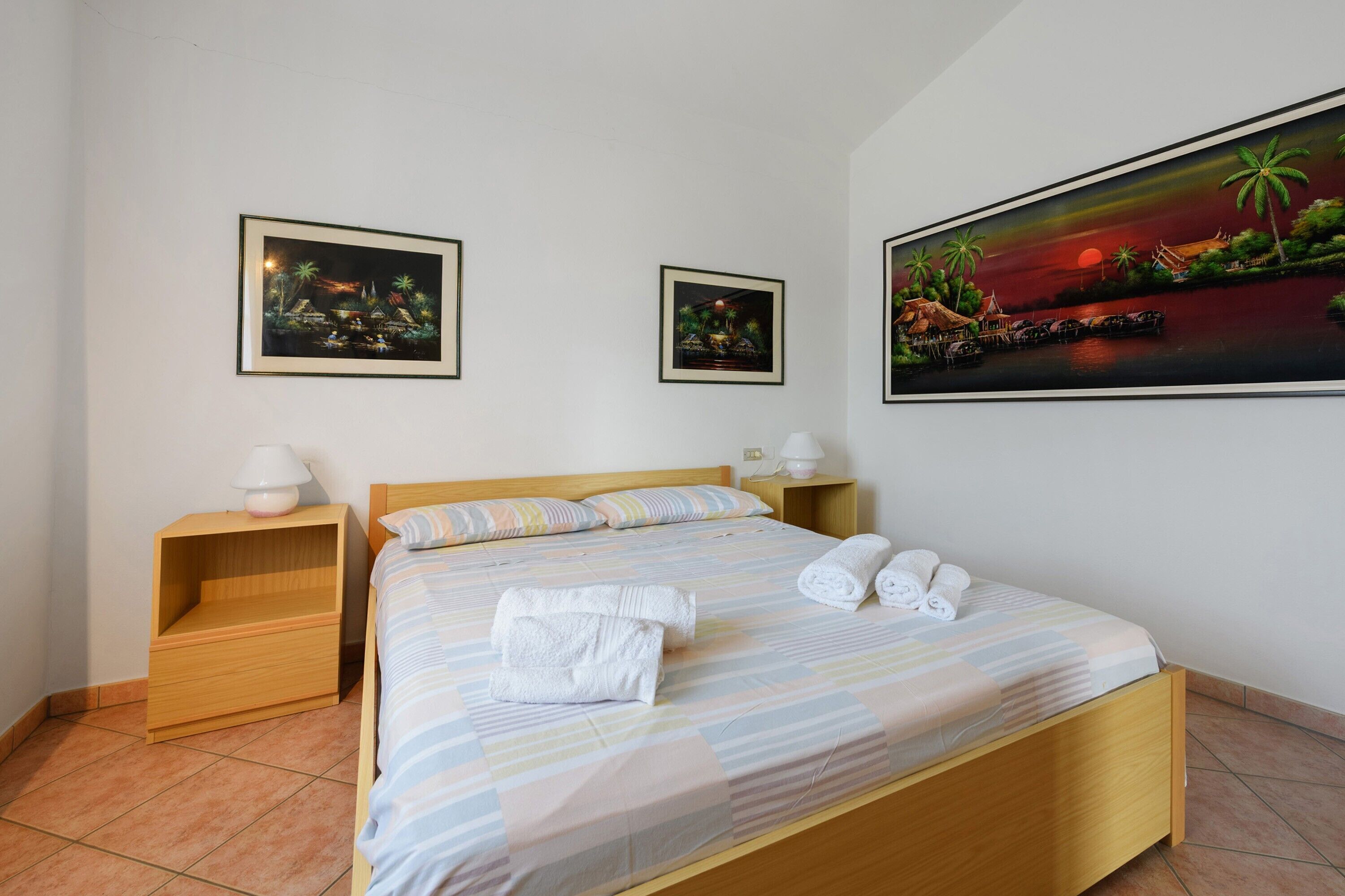 A bedroom with a bed, two nightstands, a lamp, and two framed pictures on the wall.