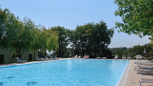 Ein rechteckiger Pool mit klarem, blauem Wasser, umgeben von weißen Liegestühlen und Bäumen.