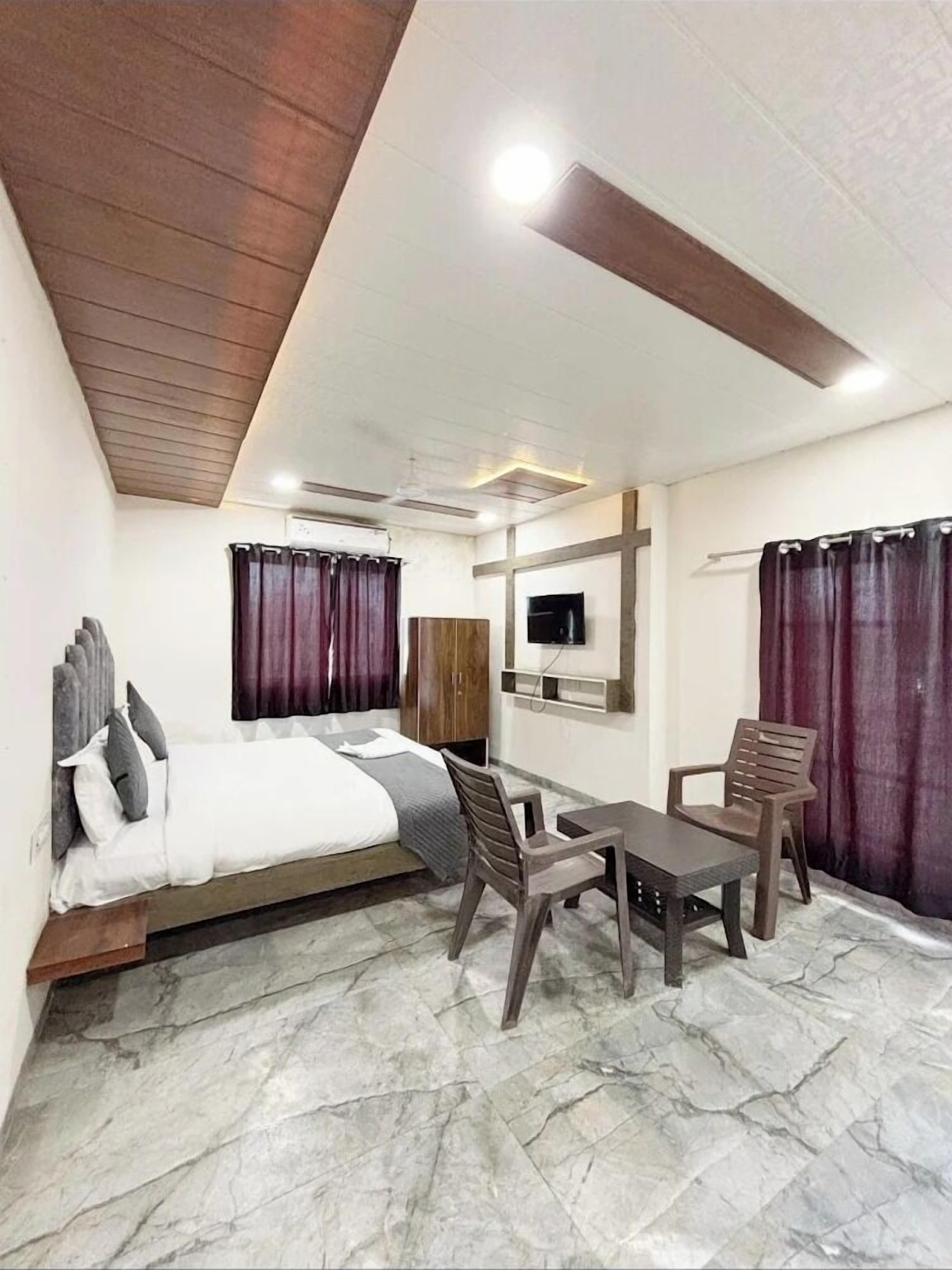 A hotel room with a bed, a TV mounted on the wall, a dining table with chairs, and a marble floor.