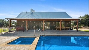 A covered outdoor pool area with a metal roof, a pool, and a patio with seating. - Spacious 12-Bedroom Resort in Graham Texas  - sleeps 40 (Graham)