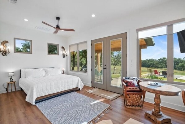 Une chambre à coucher avec un lit, un ventilateur de plafond, une grande fenêtre et une vue sur l’extérieur.
