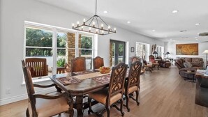 A spacious dining area with a large wooden table and chairs, surrounded by large windows offering a view of greenery. - Spacious 12-Bedroom Resort in Graham Texas  - sleeps 40 (Graham)