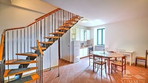 A modern kitchen with a built-in stove, a dining area with a round table and chairs, and a wooden staircase with black railings.