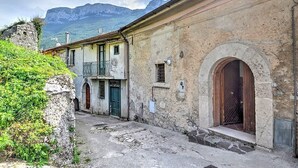 A narrow street with old buildings, a stone wall, and a mountain in the background.