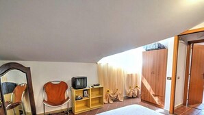 A bedroom with a large bed, a wooden wardrobe, a television on a shelf, a chair, and a mirror.