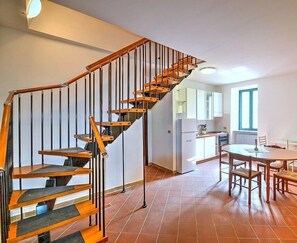 A modern kitchen with a built-in stove, a dining area with a round table and chairs, and a wooden staircase with black railings.