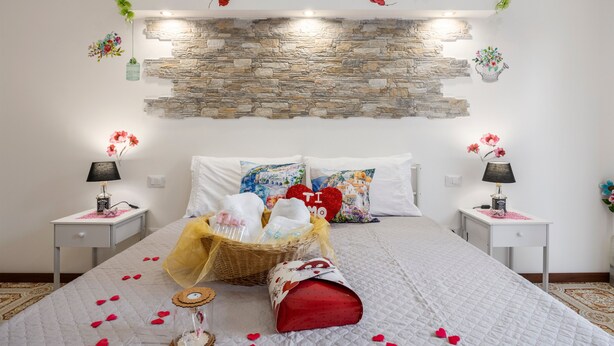 A bedroom with a stone wall, floral decorations, a bed with rose petals, and a basket of toiletries. - Guest House 'Sole e Amore' with Balcony, Wi-Fi and Air Conditioning (Casteldaccia)