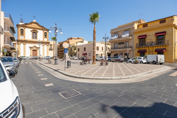 Una calle con coches estacionados, una palmera y edificios con balcones y toldos.