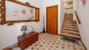 Un escalier dont les marches sont décorées d’un motif menant à une porte, une commode en bois avec un miroir et un cadre photo fixé au mur.