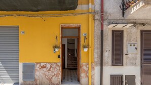 Un bâtiment jaune avec un volet fermé, une porte portant le numéro 19, et un escalier menant à l’intérieur.