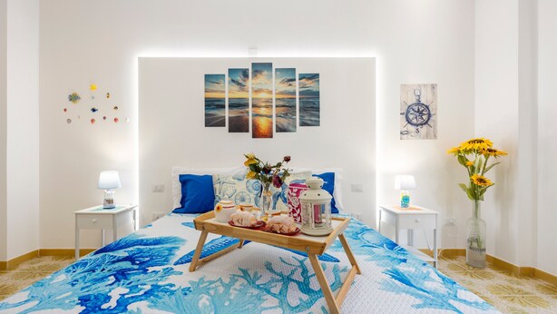 Une chambre à coucher bien rangée, avec un lit, des tables de chevet, une lampe de chevet, un plateau contenant divers objets et un vase avec des fleurs.
