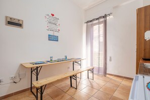 Une pièce avec une table en bois, un banc, un panneau fixé au mur et une fenêtre avec un rideau.