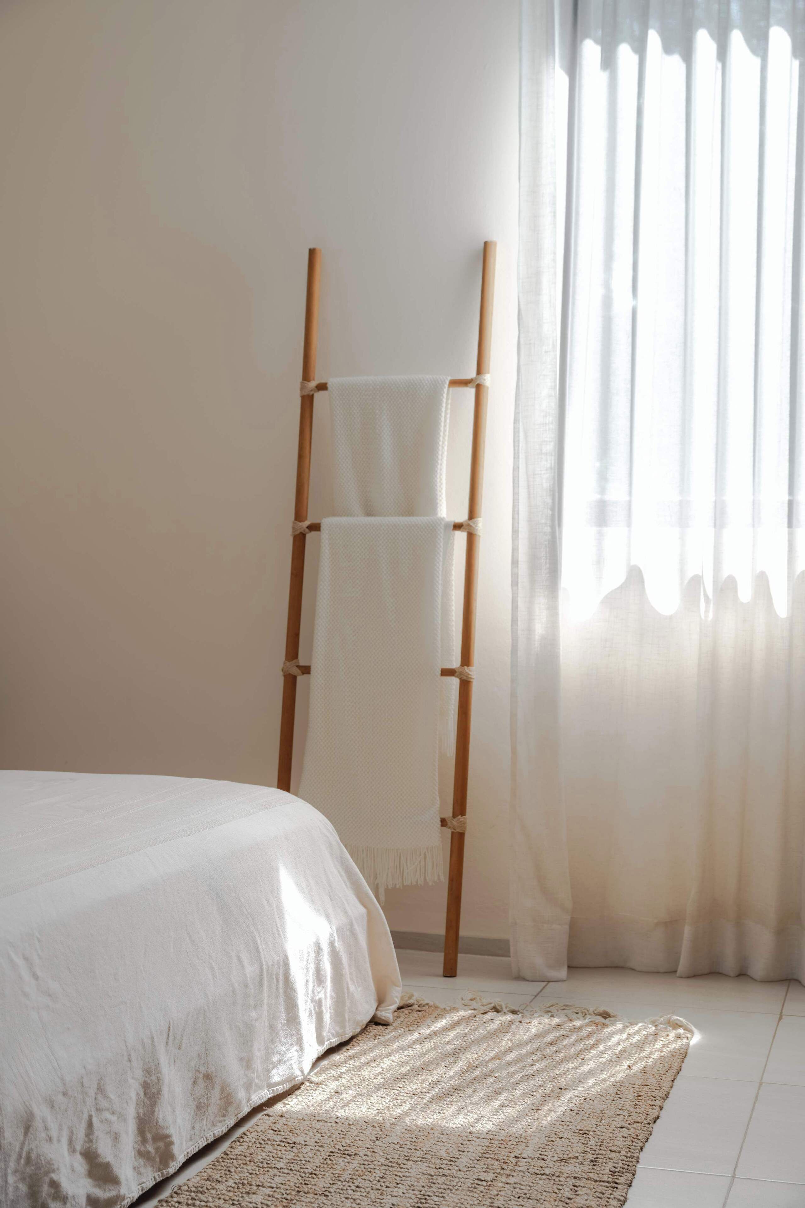A bedroom with a bed, a wooden ladder, and sheer curtains.