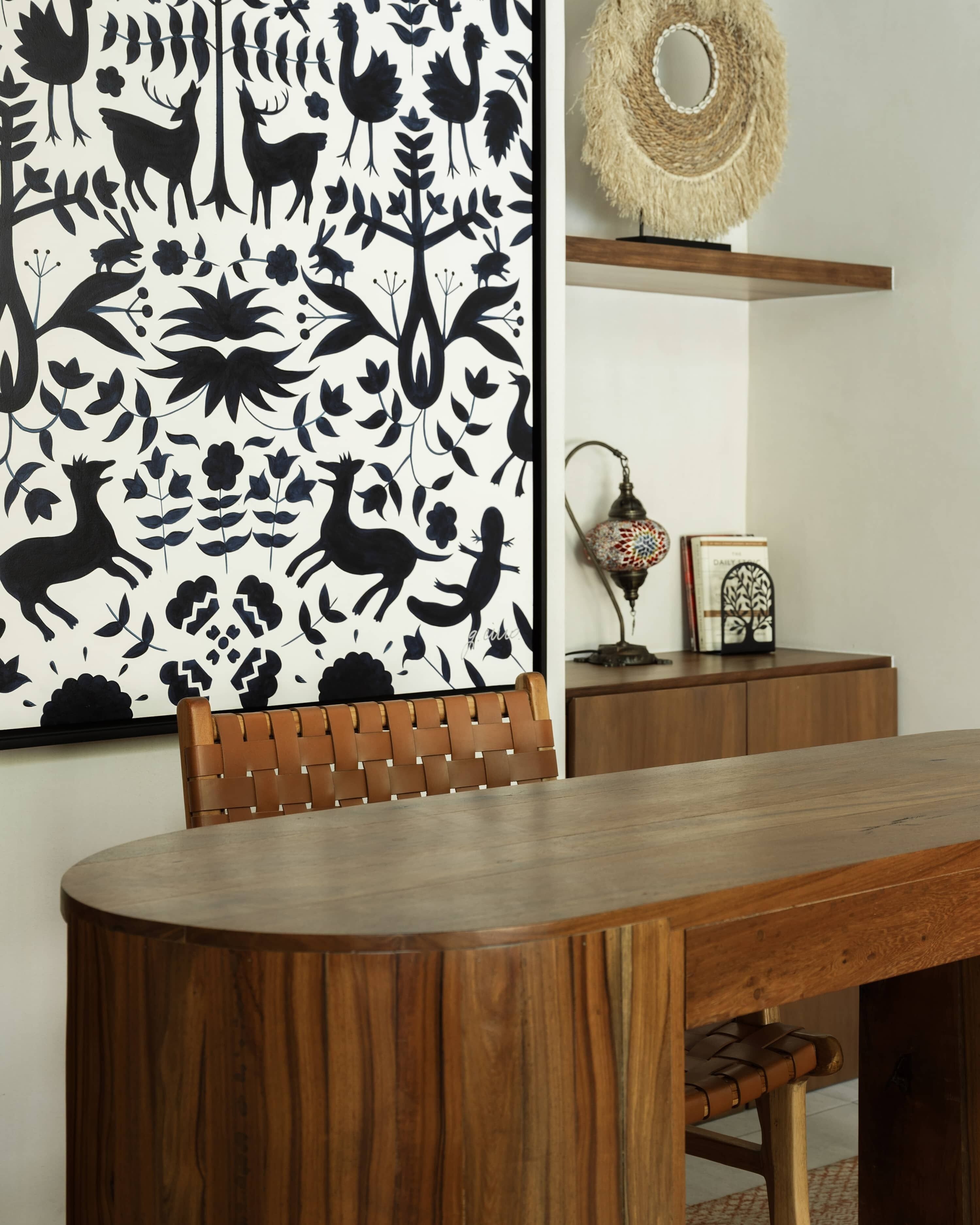 A dining area with a wooden table and chairs, a wall with a black and white animal pattern, a woven basket, and a small lamp.