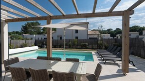 Un espace extérieur abrité comprenant une piscine, des chaises longues et une table avec des chaises.