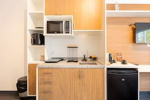 A compact kitchen with wooden cabinets, a microwave, a sink, and a black dishwasher. - Charming studio in São Caetano ap110 (São Caetano do Sul)