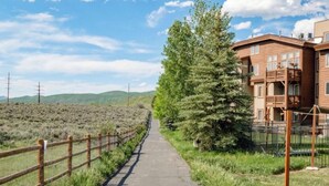 A pathway leading to a building with a balcony, surrounded by greenery and hills. - Park City / Kimball Junction - 2-bed 2-bath Condo - Free Covered Parking, AC (Park City)