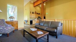 A living area with a sofa, coffee table, and patterned armchair. A kitchen is visible in the background. - Park City / Kimball Junction - 2-bed 2-bath Condo - Free Covered Parking, AC (Park City)