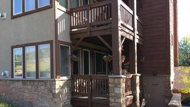 A two-story house with a stone foundation, a wooden deck with railings, and a front door. - Park City / Kimball Junction - 2-bed 2-bath Condo - Free Covered Parking, AC (Park City)