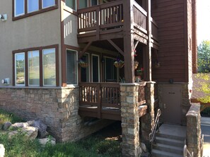 A two-story house with a stone foundation, a wooden deck with railings, and a front door.