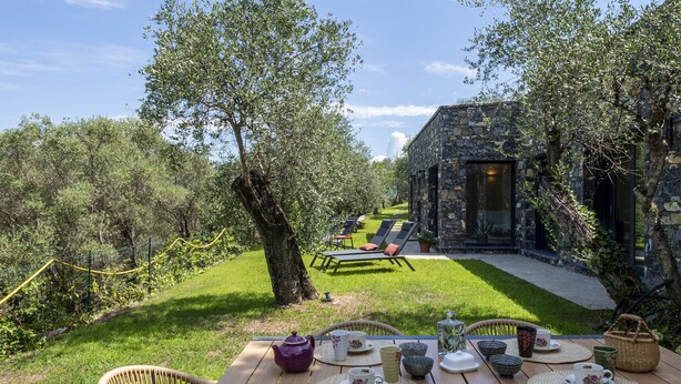 A wooden table set with tea and cups, overlooking a stone building and a grassy garden with chairs and a lounge area. - Olivuzza a Santa Margherita by Wonderful Italy (Santa Margherita Ligure)