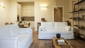 A living room with a white sofa, a coffee table with books, and a kitchen in the background. - Olivuzza a Santa Margherita by Wonderful Italy (Santa Margherita Ligure)