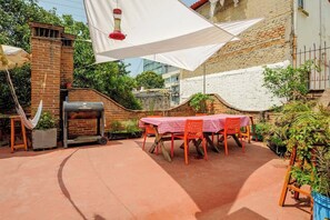 An outdoor patio with a brick barbecue, a table with chairs, and umbrellas providing shade.