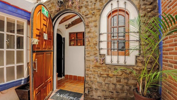 A stone building with a wooden door, a window with a metal grille, and a welcome mat. - Casa Aimee - Suite B · Casa Aimee, High-up Suite (Mexico City)
