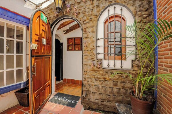 A stone building with a wooden door, a window with a metal grille, and a welcome mat.