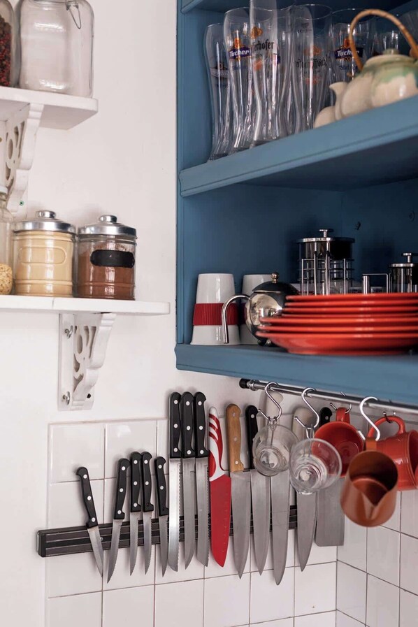 A kitchen with a knife rack, a shelf with glass jars, and a blue cabinet with glassware.