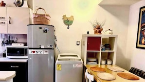 Une cuisine compacte équipée d’un réfrigérateur, d’un four à micro-ondes et d’un petit four. On y trouve une table à manger avec des assiettes et un panier posé sur le comptoir.