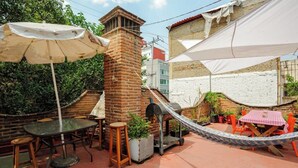 Een terras buiten met een bakstenen schoorsteen, een hangmat en een tafel met stoelen.
