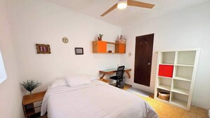 Een slaapkamer met een bed, een bureau, een stoel, een kledingkast en een plafondventilator.