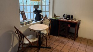 Una pequeña cocina con ventana, cafetera, una mesa y dos sillas.